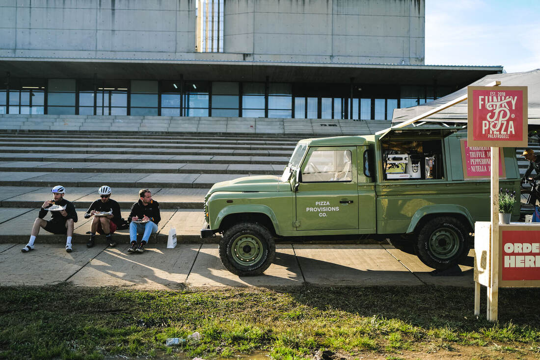 Ciclistas comiendo pizza junto al Land Rover de Pizza Provisions Co. en The Traka
